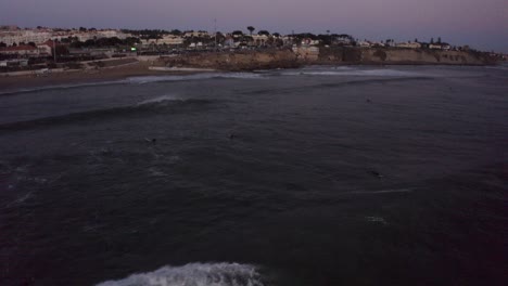 Surfer-takes-off-riding-long-board-wave-in-San-Pedro-Cascais,-aerial-tracking-at-dusk