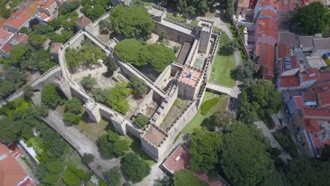 Sao-Jorge-castle-Lisbon-Portugal,-drone-rises-and-tilts-down-above-city