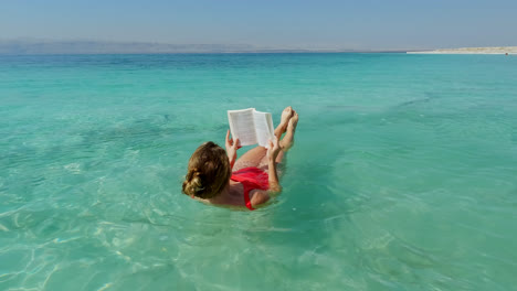 Beautiful-Young-Woman-Floats-in-the-Dead-Sea-in-Red-Swimsuit-while-Reading-Book
