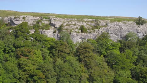 Drohnenaufnahmen,-Die-Seitwärts-Fliegen-Und-über-Einen-Steilen,-Von-Bäumen-Gesäumten-Kalksteinfelsen-Aufsteigen,-Zeigen-Die-Landschaft-Von-Yorkshire-Mit-Ackerland,-Feldern,-Steinmauern-Und-Der-Hügeligen-Landschaft-In-Der-Ferne