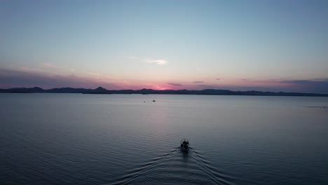 Das-Boot-Fährt-Hinaus-Aufs-Meer,-Während-Im-Morgengrauen-Der-Rosafarbene,-Blaue-Stundenton-Den-Horizont-Erhellt