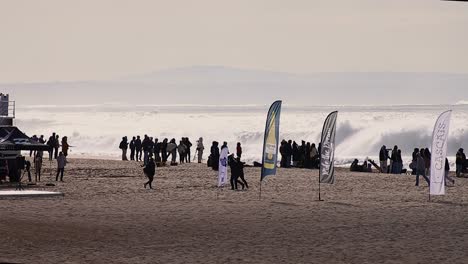 Surfing-competition-with-tall-flags-on-beach-as-onlookers-watch-to-the-crashing-waves