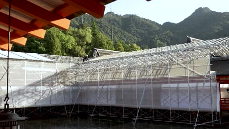 Gerüst,-Das-Einen-Teil-Des-Itsukushima-Schreins-Bedeckt,-Mit-Arbeitern,-Die-Auf-Dem-Dach-Renovierungsarbeiten-Durchführen