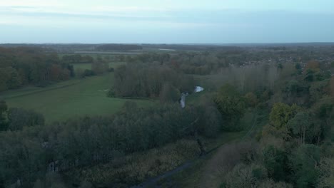 Zipline-aerial-drone-shot-of-the-lush-green-trees,-winding-rivers,-verdant-fields,-and-a-nearby-village-in-Breckland-district,-Norfolk-county,-in-the-east-of-London,-United-Kingdom