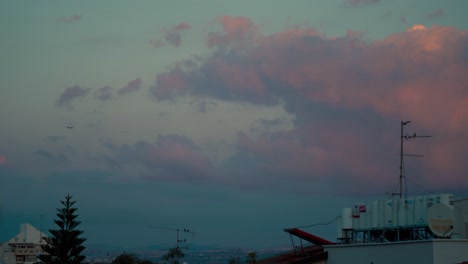 Eine-Atemberaubende-Wolkenbewegung-Während-Des-Sonnenuntergangs-über-Den-Gebäudedächern,-Fliegende-Vögel-Und-Ein-Flugzeug,-Bunter-Himmel,-Naher-Osten,-Tel-Aviv,-Israel,-Sony-4K-Video