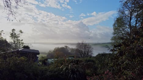 A-blue-sky-overhead-and-white-fluffy-clouds-and-an-early-morning-autumn-mist-over-the-Tamar-estuary-in-the-county-of-Devon-in-the-UK