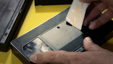Applying-a-white-label-on-a-VHS-tape,-with-the-handwritten-text-1990s