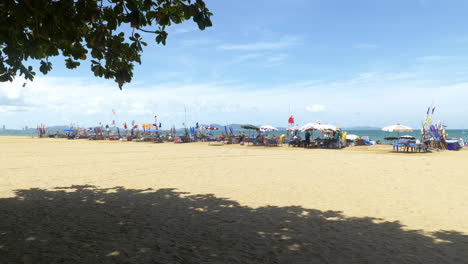 Beachfront-footage-taken-from-under-the-shades-of-trees-capturing-a-line-of-beach-canopies-with-colorful-banners-overlooking-the-sea-and-mountains