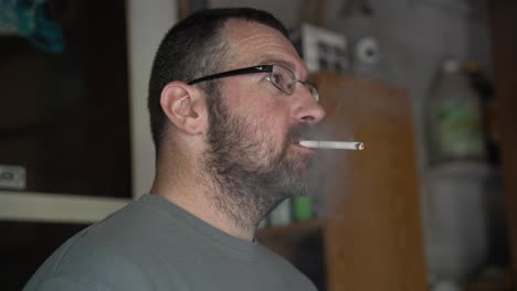 A-caucasian-man-with-glasses-lights-a-cigarette-and-breathes-out-smoke