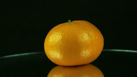 Eine-Einzelne-Orange-Dreht-Sich-Auf-Einem-Verspiegelten-Sockel-Vor-Schwarzem-Hintergrund