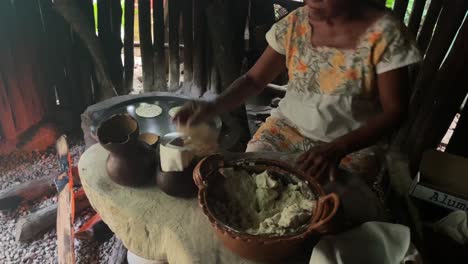 woman-making-corn-tortillas-by-hand-in-her-rustic-outdoor-kitchen-on-a-makeshift-comal-that-uses-a-oil-barrel-lid-over-an-open-wooden-fire