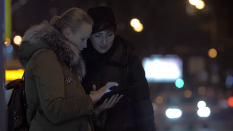 Freundinnen-Benutzen-Tablet-PC,-Während-Sie-Auf-Der-Straße-Auf-Den-Bus-Warten