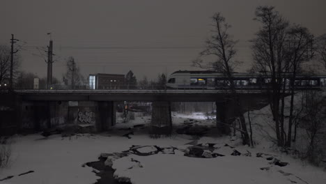 Evening-view-of-passenger-train-running-across-the-bridge-in-winter-city