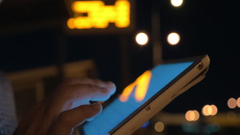 Man-working-with-touch-pad-on-bus-stop-at-night