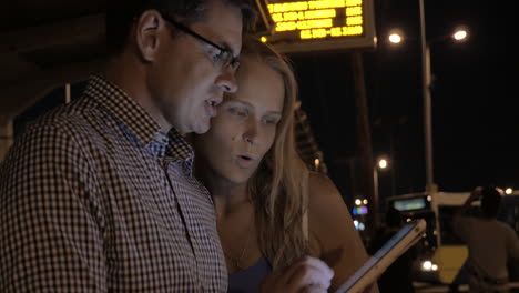 Junges-Paar-Mit-Tablet-PC-An-Der-Bushaltestelle-In-Der-Nacht