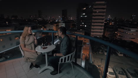 Man-and-woman-having-drinks-on-the-rooftop-cafe-in-night-city