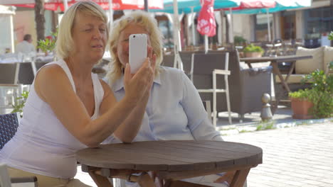 Senior-women-friends-taking-selfie-in-street-cafe