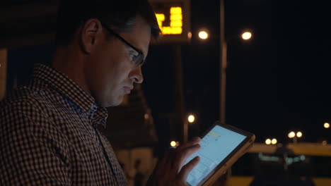 Man-with-tablet-computer-on-bus-station-at-night