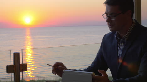 Smoking-business-man-working-with-touch-pad-in-seaside-cafe
