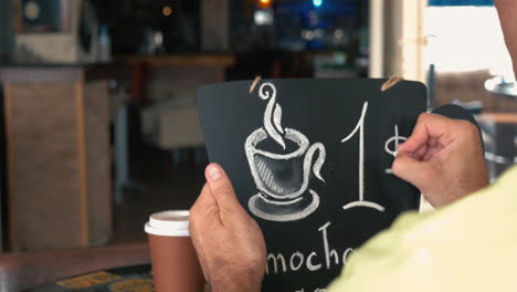 Man-writing-coffee-price-on-chalk-board