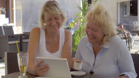 Zwei-ältere-Frauen-Schauen-Sich-Fotos-Auf-Einem-Block-Im-Straßencafé-An