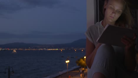 Woman-with-pad-on-hotel-balcony-at-night