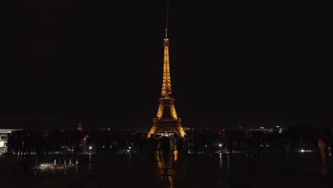 Toy-Sellers-Selling-Miniature-Eiffel-Tower-in-Front-of-Real-One-at-Night-in-Place-du-Trocadero