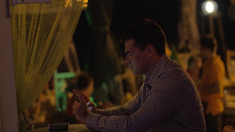 Man-with-mobile-phone-in-street-cafe-at-night