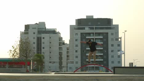 Young-professional-skateboarder-performing-trick-in-an-urban-city-landscape,-buildings-in-the-background
