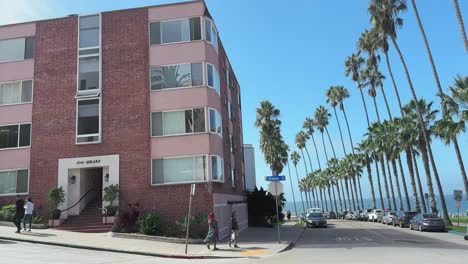 Street-in-La-Jolla-with-palm-trees,-coastal-ocean-view,-buildings-and-people