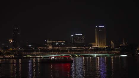 Nächtliches-Stadtbild-Der-Marina-Bay-Mit-Der-Jubiläumsbrücke-In-Der-Stadt-Singapur-Und-Vorbeifahrenden-Transportbooten