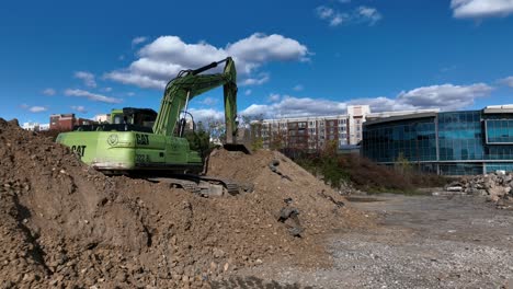 A-low-angle-view-of-a-lime-green-excavator-on-a-construction-site,-on-a-mound-of-dirt,-on-a-sunny-day-with-blue-skies