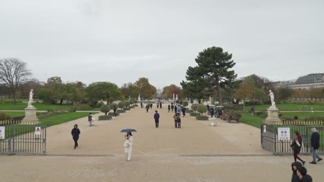 Parisinos-Caminando-En-El-Jardín-De-La-Place-Du-Carrusel-Con-El-Arco-Del-Triunfo-En-La-Distancia