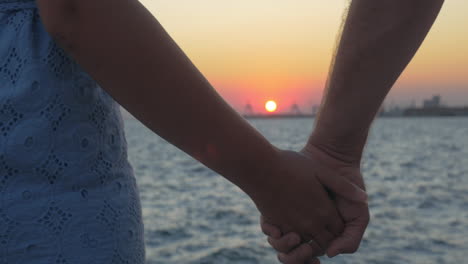 Close-up-shot-of-romantic-couple-holding-hands-on-the-beach-against-sunset-Piraeus-Greece