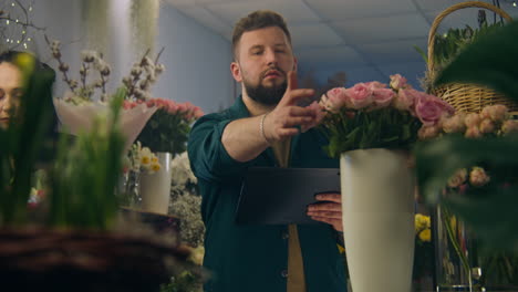Der-Männliche-Florist-Zählt-Die-Blumen-In-Der-Vase-Und-Nimmt-Die-Bestellung-Per-Tablet-Entgegen