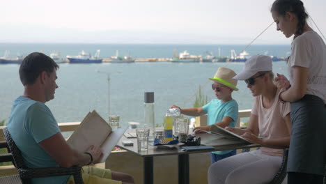 On-the-sea-coast-of-city-Perea-Greece-a-young-family-sits-in-cafe