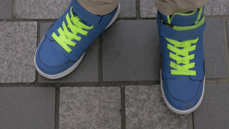 Kid-feet-in-blue-trainers-on-paved-sidewalk