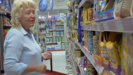 Ältere-Frau-Wählt-Dosenfutter-Für-Haustiere-Im-Supermarktgang-Mit-Einkaufskorb-Aus