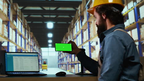 Warehouse-manager-looks-at-greenscreen-on-smartphone
