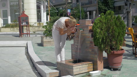 Young-woman-washing-her-face-in-public-fountain-on-the-street-at-summer-Piraeus-Greece