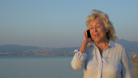 En-La-Costa-Del-Mar,-La-Ciudad-De-Perea,-Grecia,-Es-Una-Mujer-Caminando-Y-Hablando-Por-Teléfono-Móvil.