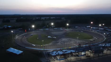 Cars-speeding-around-race-track-during-sunset,-aerial-view