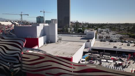 Petersen-Automotive-Museum-panning-right-aerial-drone-view-of-the-side-of-the-building-with-people-walking-around-at-a-car-show