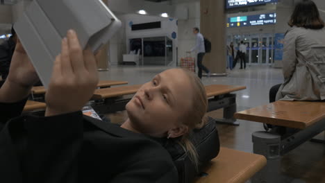 Woman-with-pad-lying-on-the-bench-in-airport-terminal
