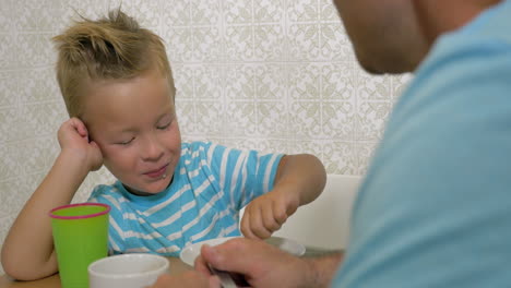 Son-speaking-with-father-and-eat-using-a-spoon-and-smiling