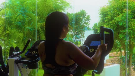 Profile-shot-of-brunette-long-hair-asian-young-woman-in-sport-clothes-walking-in-treadmill-and-smiling-at-gym-in-luxury-resort-hotel-at-daytime