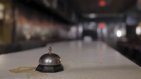 Close-up-of-a-woman's-hand-ringing-a-call-bell-on-a-stained-countertop-at-an-old-restaurant