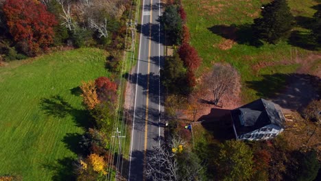 A-high-angle-aerial-view-over-a-country-road-with-colorful-trees-around-on-a-sunny-day-in-autumn