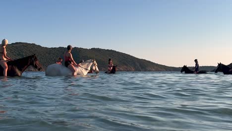 Tourists-enjoy-bathing-while-riding-bareback-horses-in-sea-water-during-summer-season