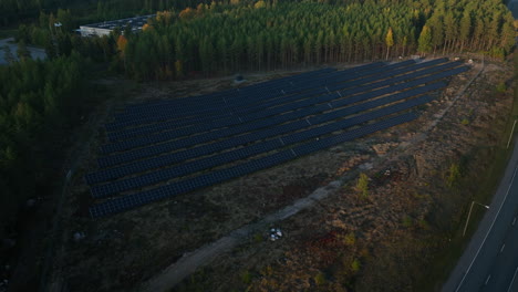 Aerial-view-circling-a-solar-field-in-middle-of-fall-forest-and-a-road